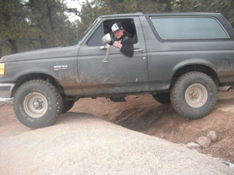 1990 Ford Bronco - A gray Ford Bronco navigates a rocky trail, with the driver looking out the window.