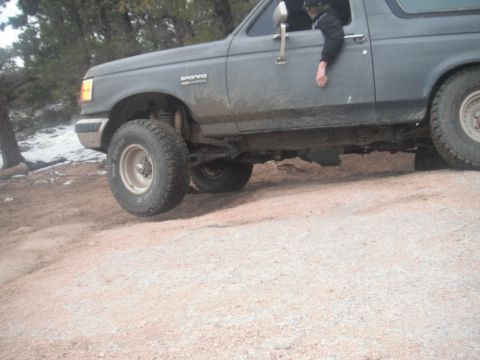 1990 Ford Bronco - This Ford Bronco is navigating a rough, unpaved road with scattered snow.