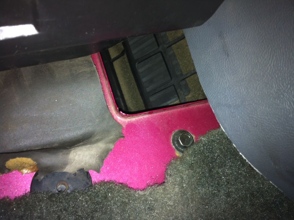 Pink floor pan with worn carpet under a vehicle dash