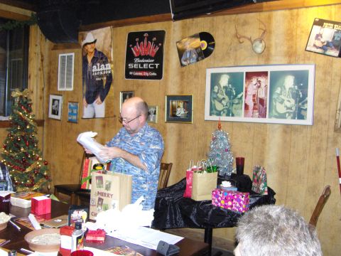 2007 Ford Mustang - A man unwraps a gift during a Christmas party, surrounded by festive decorations and memorabilia on the walls.
