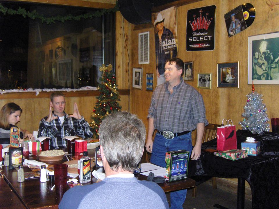 People gathered around a table at a holiday party, with Christmas trees and posters on the wall