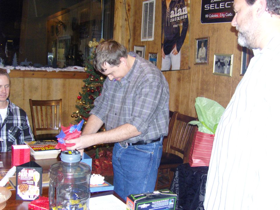 People gathered around a table with a Christmas tree and gifts, with posters on the wall