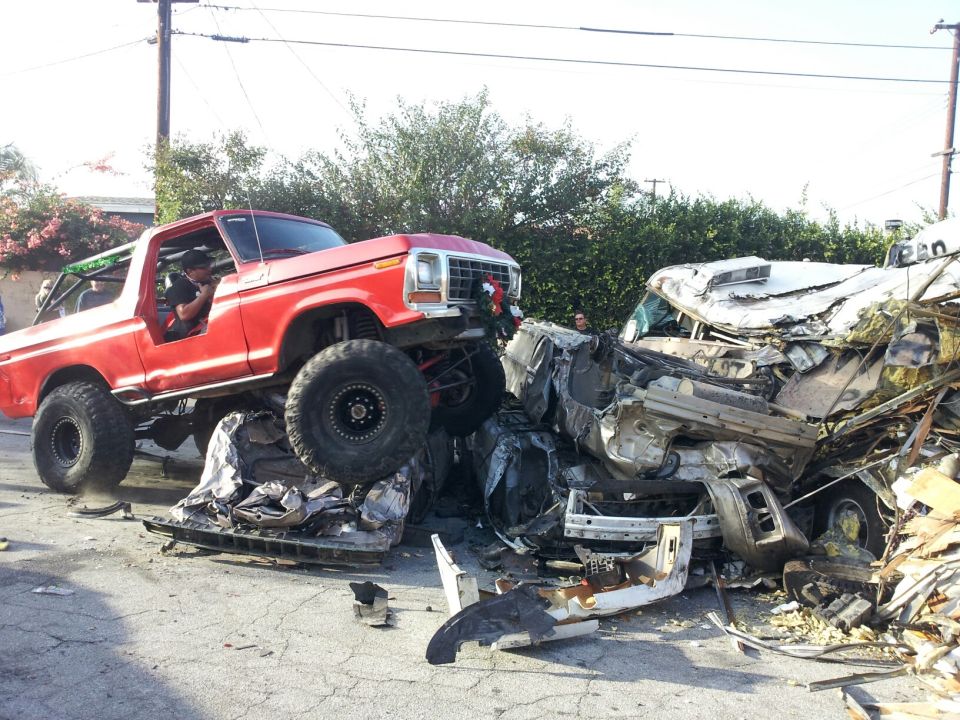 Red 1978 Ford Bronco with large tires on top of a severely damaged white car