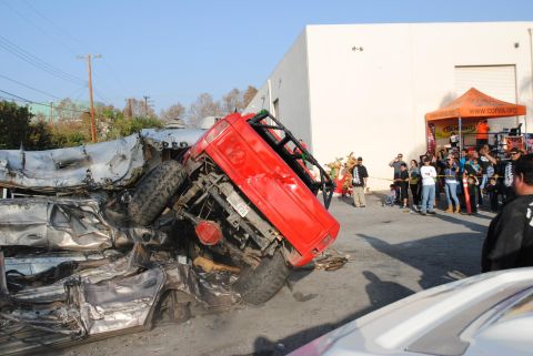 1978 Ford Bronco - A red off-road vehicle is piled on top of severely damaged cars, with onlookers present.