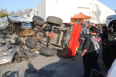 1978 Ford Bronco - An overturned red SUV lies on its side amidst debris, with onlookers gathered around.