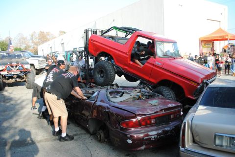 1978 Ford Bronco - A red 1978 Ford Bronco is being lifted by a forklift, crushing a damaged car beneath it.