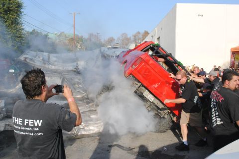 1978 Ford Bronco - A red off-road vehicle is shown crushing another vehicle while onlookers film the event.