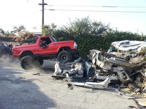1978 Ford Bronco - A red 1978 Ford Bronco jumps over a wrecked vehicle, creating a dramatic scene of destruction.