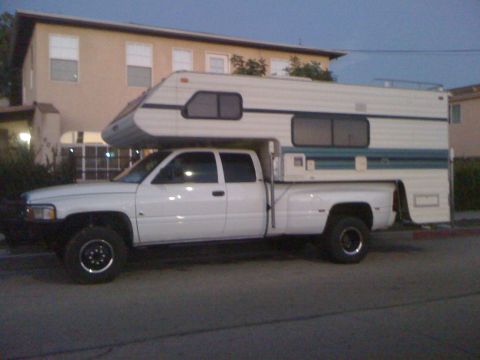 1997 Dodge 3500 - A white pickup truck is fitted with a large camper shell, extending over the bed and cab.