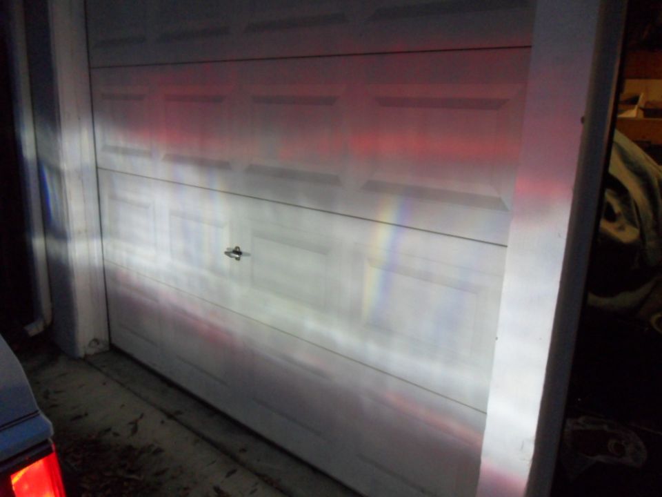 headlights shine on a white garage door, casting red and white light patterns
