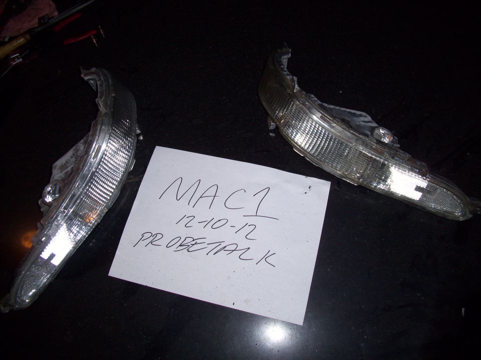 Two clear plastic car light assemblies with textured lenses on a dark surface