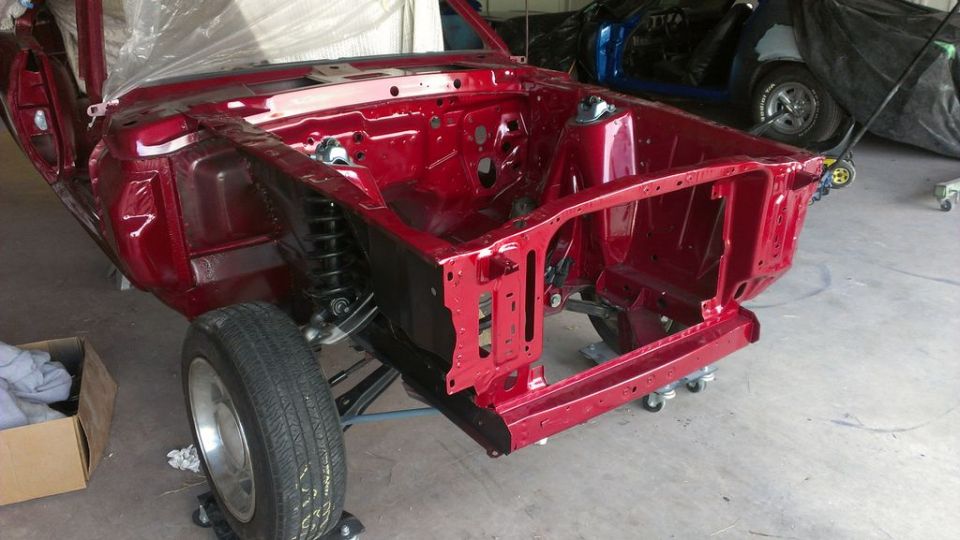 Red 1970 Ford Mustang frame, front view. Another car covered in background