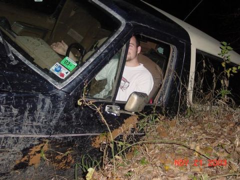 1989 Ford Bronco - A man is inside a dirty vehicle that appears to be stuck in the mud and foliage.