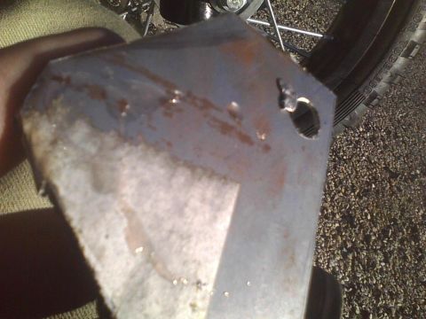 2003 Ford Crown Victoria - A metal bracket with a hole is shown, with a tire and gravel in the background. The Supermotors.net logo is visible.