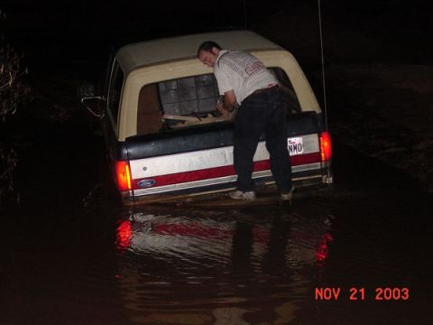1989 Ford Bronco - A 1989 Ford Bronco is partially submerged in water, with a person standing in the tailgate area.