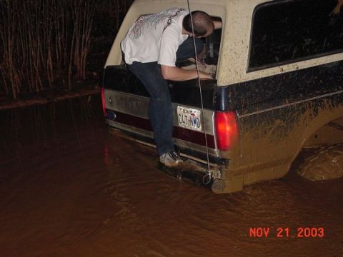 1989 Ford Bronco - Ford Bronco stuck in mud, with a person exiting the vehicle.