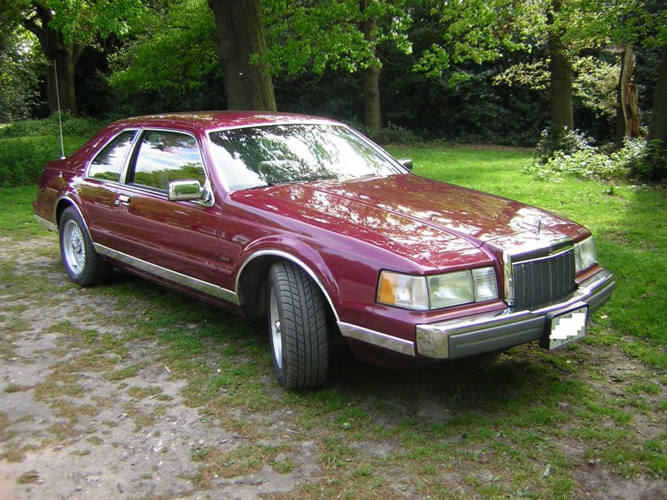Maroon Lincoln Mark VII parked on grass with trees in background