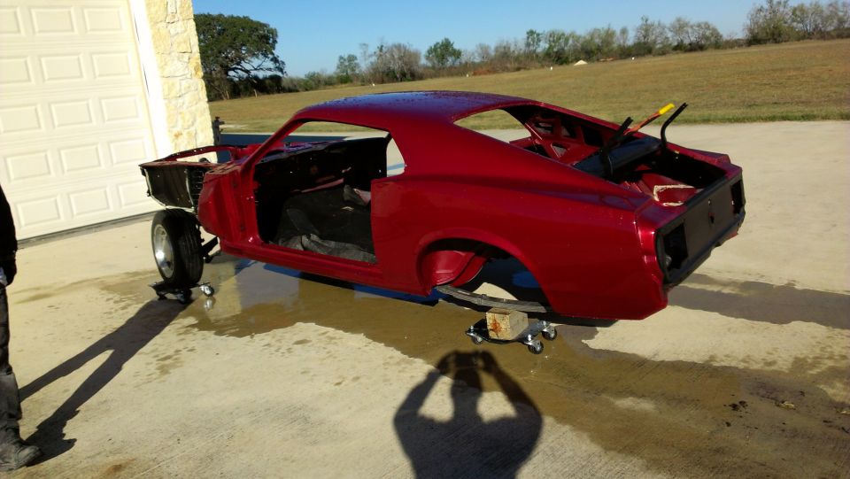 Red 1969 Mustang body on jack stands outside garage, undergoing restoration