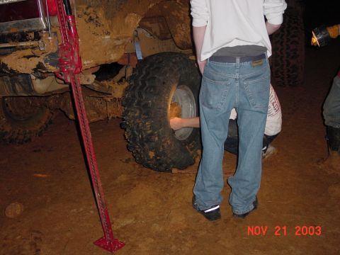 1989 Ford Bronco - A vehicle is stuck in the mud, and people are attempting to change a tire.