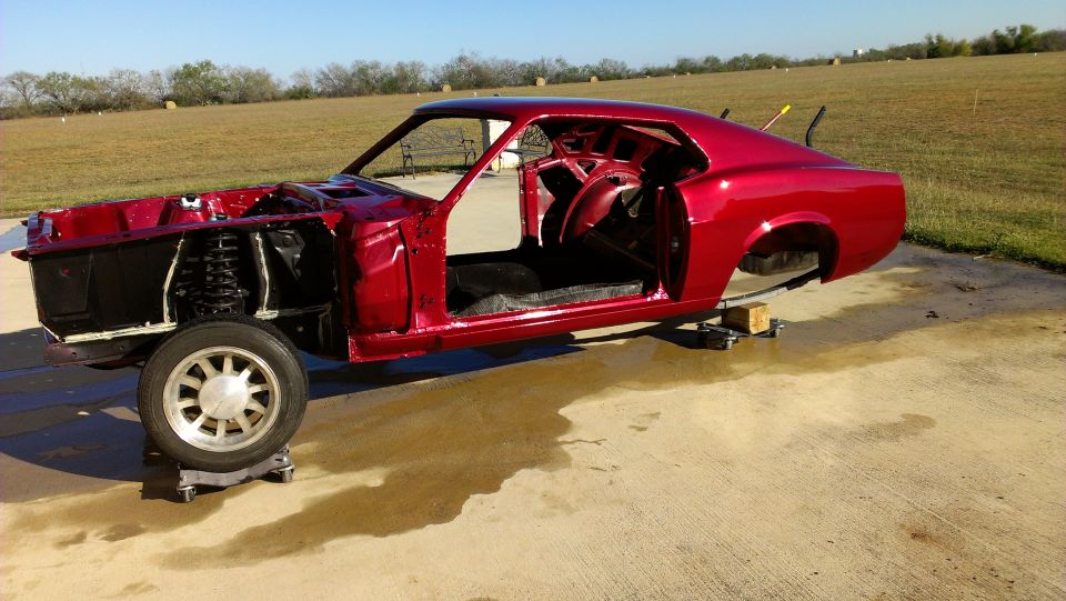 Red 1970 Ford Mustang body on a concrete pad, stripped down for restoration