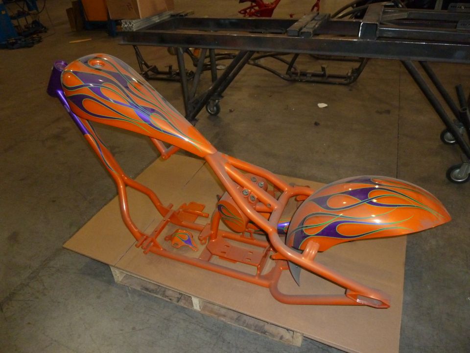 Orange motorcycle frame and fender with purple and yellow flame graphics, on a pallet