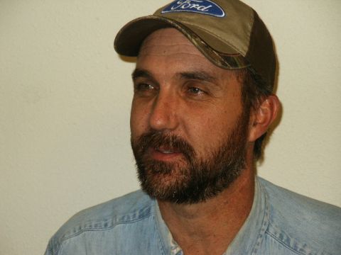 1990 Ford Bronco - A man with a beard wears a Ford baseball cap and a denim shirt.