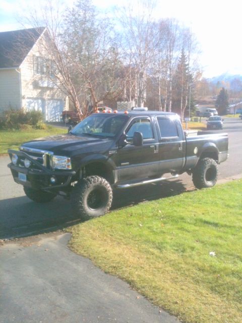 1990 Chevrolet Suburban - This lifted pickup truck is parked on the side of a road in a suburban neighborhood.