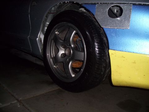 1995 Ford Probe - A close-up view of a car's wheel and fender reveals a two-tone paint job and a metal patch.