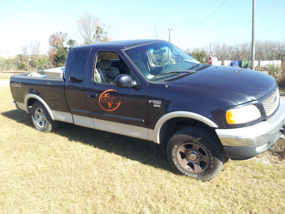 Dark blue and tan Ford F-150 pickup truck with a CRA logo on the door, parked on grass