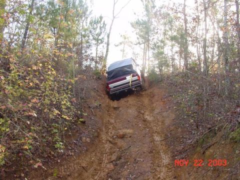 1989 Ford Bronco - A maroon Ford Bronco navigates a steep, muddy trail surrounded by autumn foliage.