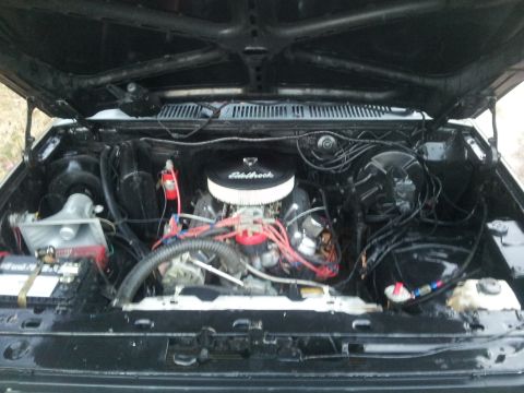 1986 Ford Bronco - The engine bay of a vehicle is shown with the hood open, revealing the motor and its components.
