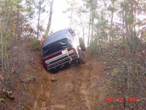1989 Ford Bronco - A 1989 Ford Bronco navigates a steep, muddy trail surrounded by trees.