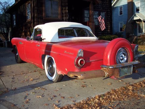 1956 Ford Thunderbird - A red 1956 Ford Thunderbird convertible with a white top and continental kit is parked in front of a house.