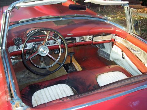 1956 Ford Thunderbird - The interior of a classic red convertible shows wear on the seats and dashboard.