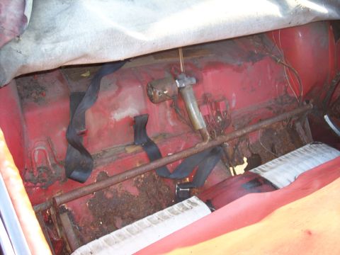 1956 Ford Thunderbird - The rear interior of a car shows significant rust and wear on the floor and seat mounts.