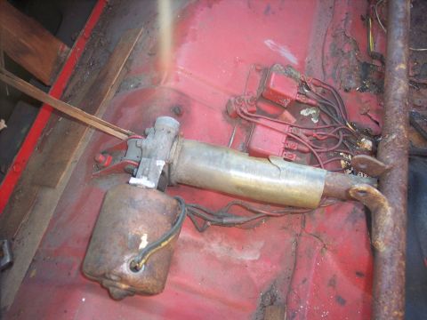 1956 Ford Thunderbird - Close-up of a power window mechanism with visible rust and wiring on a red interior floor.