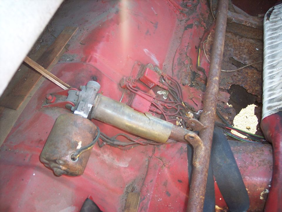 Interior view of a rusty car floor with a fuel pump and wiring
