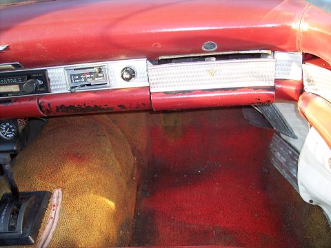 1956 Ford Thunderbird - The interior of a classic car shows a red dashboard with a radio and a textured glove compartment panel.