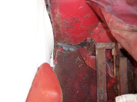 1956 Ford Thunderbird - Close-up view of a corroded car interior floor, revealing extensive rust damage and worn carpeting.