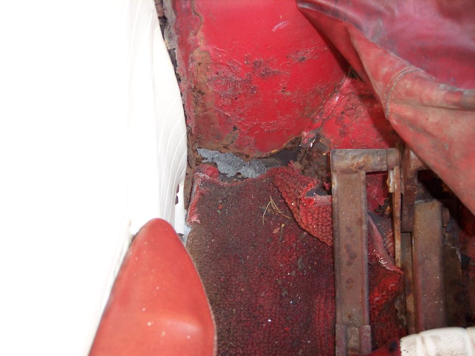 Red car interior floor with significant rust and damage, showing worn red carpet and metal supports