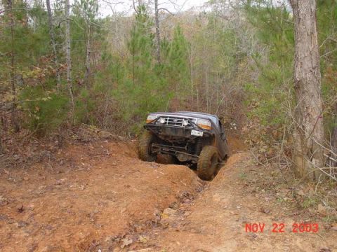 1989 Ford Bronco - A modified Ford Bronco is shown tackling a challenging off-road course with steep inclines and muddy terrain.