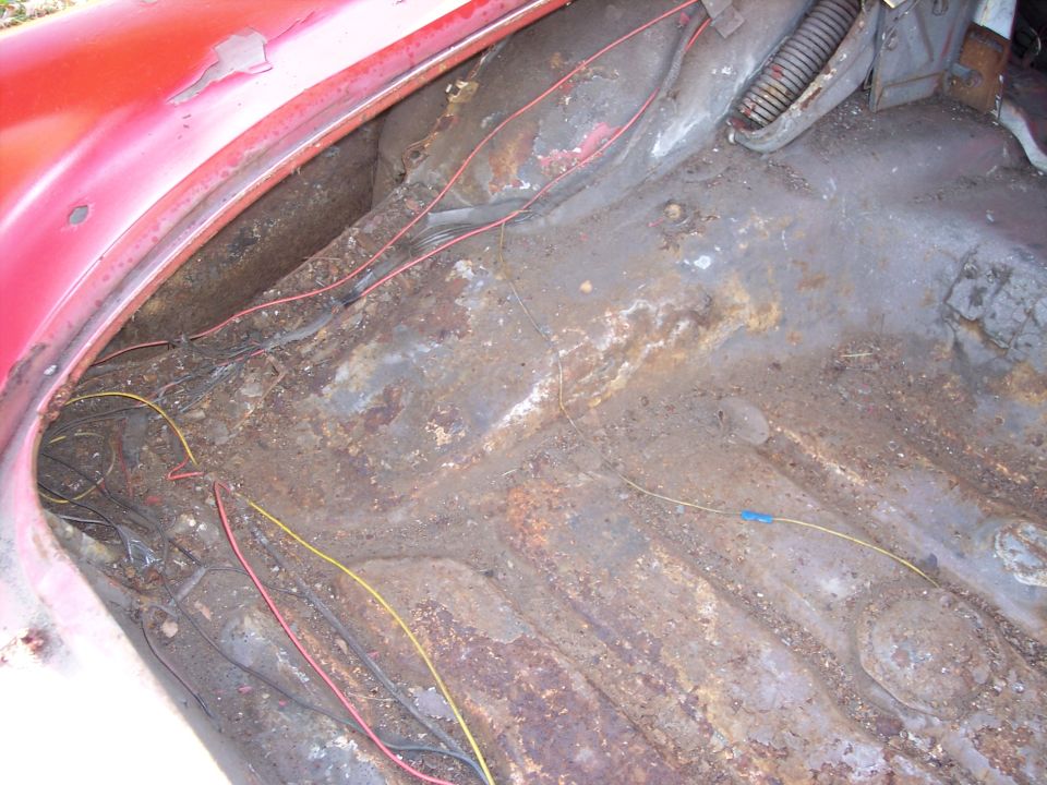 Red car trunk interior with extensive rust and exposed wiring
