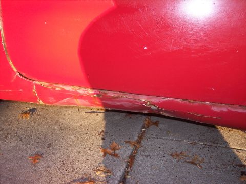 1956 Ford Thunderbird - The lower portion of a red car door exhibits significant rust and damage.