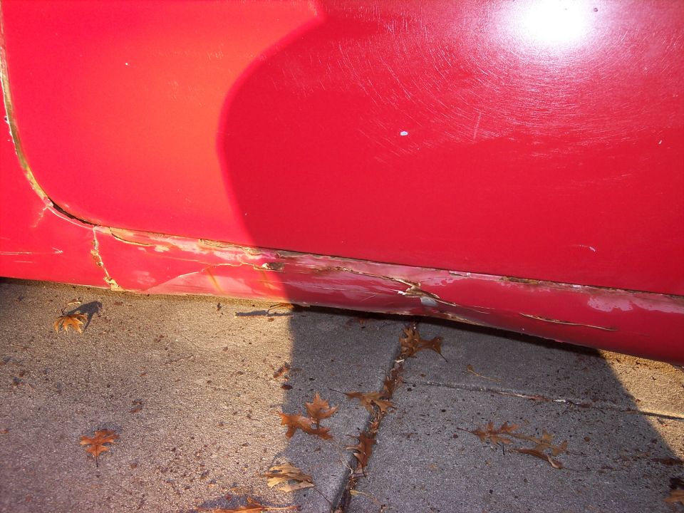 Red car door bottom showing rust and damage