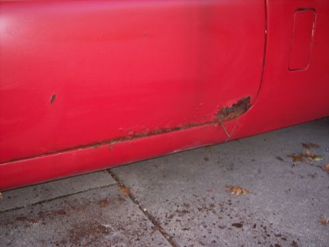 1956 Ford Thunderbird - The lower portion of a red car door shows extensive rust and corrosion.