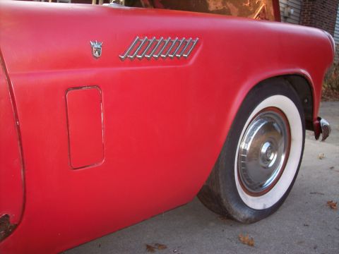 1956 Ford Thunderbird - Close-up of a red car's side fender and wheel, revealing a flat tire and vintage styling details.