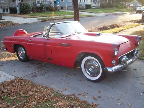 1956 Ford Thunderbird - A classic red convertible sits parked on a concrete driveway, with fallen leaves scattered around.