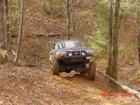 1989 Ford Bronco - 1989 Ford Bronco navigates a muddy, wooded off-road path.