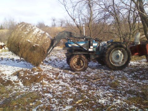 1987 Ford F-250 - A tractor moves a large hay bale in a field with patchy snow.