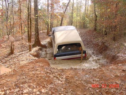 1989 Ford Bronco - A vehicle is stuck in mud on a trail surrounded by trees in the fall.